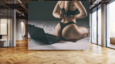 A young webcam model girl is sitting in front of a laptop. She communicates on a white bed in the bedroom. Wall mural