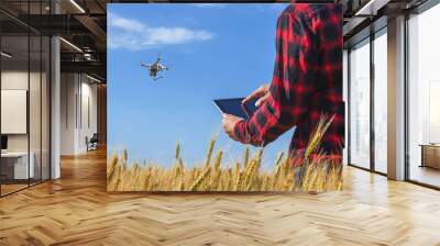 Businessman is on a field of ripe wheat is holding a Tablet computer and controls the quadrocopter. The concept of the agricultural business. Wall mural