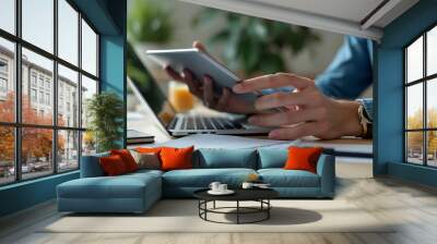 Close-up of professionals collaborating with a tablet and laptop in a modern office. The scene includes a coffee cup, eyeglasses, and documents, highlighting a productive work environment. Wall mural