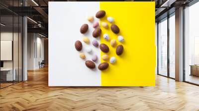 Easter colorful flat lay. Easter chocolate eggs in egg shape of vibrant colors on bright yellow and white background.  Culture food and easter celebration horizontal  flat lay. Wall mural