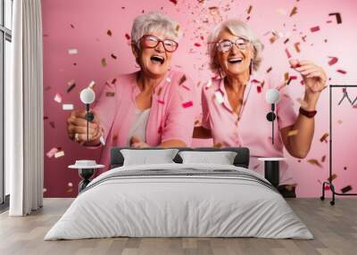 happy two senior women celebrating New Year at party with confetti on pastel pink background. Female couple. Birthday celebration.  Wall mural