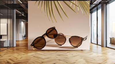 Two pairs of women sunglasses on beige background with golden palm leaves. Minimalism, summer fashion concept. Trendy sunglasses still life. Optic store discount, sale. Close up, vertical Wall mural