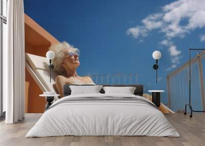 senior retired woman in summer outfit sunbathing lying on sun bed on the balcony of hotel on sunny day with blue sky Wall mural