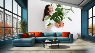 Young millennial woman holding a pot with green monstera house plant. Horizontal photo. Urban jungle green indoor gardening hobby. Wall mural