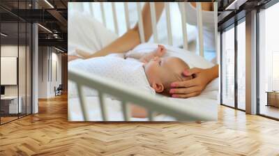 Mother sits near the crib of the newborn 2 month old baby and smiles at him Wall mural