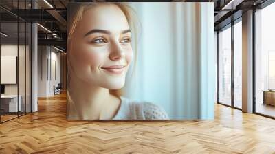 A young beautiful girl is happy about the new day, smiling and looking out the window in the morning Wall mural