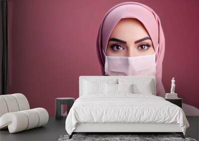 Pretty young Arab woman doctor in a mask wearing a hijab headscarf, portrait isolated on pink flat background. Banner template with copy space for text. Wall mural