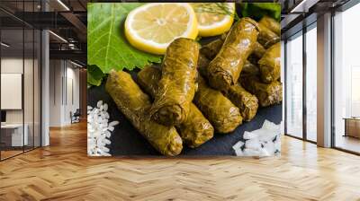 Delicious stuffed grape leaves (the traditional dolma of the mediterranean cuisine) on black dish with leaves, lemon slices, rice, parsley, dill and onion Wall mural