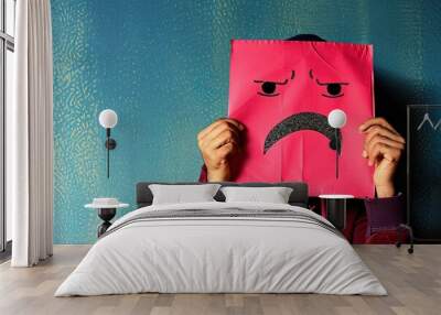 A person is holding a pink paper with a frowning face on it Wall mural