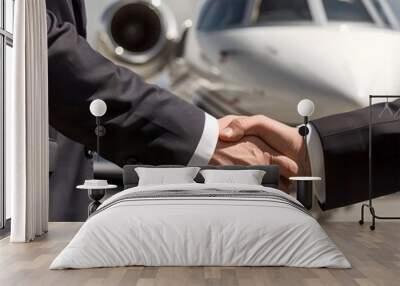 Close up of two business people shaking hands in front of a private jet Wall mural