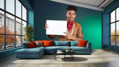 A happy young man is holding and displaying a signboard or placard on a dark background. Wall mural