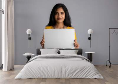 A young girl or businesswoman holding a signboard in her hands on a gray background. Wall mural