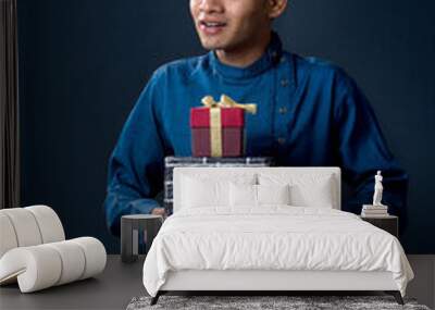 Young happy smiling handsome man holding gift box and posing on dark background Wall mural