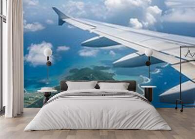 View from a plane window of a wing over an island with turquoise ocean, white clouds in the blue sky Wall mural