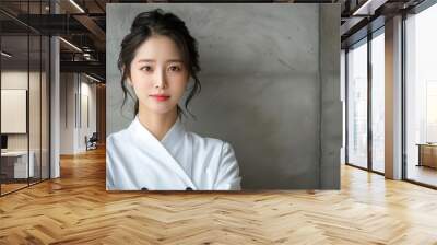 A young chef poses with confidence against a concrete wall, wearing a white chef's coat, showcasing her passion for culinary arts and professionalism in a contemporary kitchen atmosphere. Copy space Wall mural