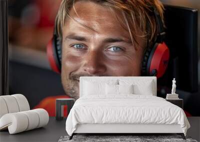 A young male call center employee wearing a red shirt and headphones with a microphone smiles at the camera. He has blond hair and blue eyes. The background is blurred Wall mural