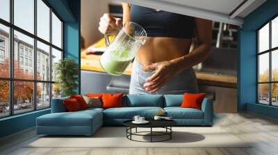 Fitness diet concept. Sporty woman drinking a green detox smoothie for breakfast in the kitchen. Wall mural