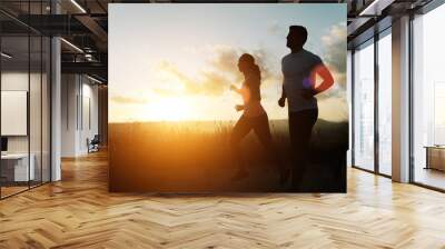 Two athletes running at sunset. Backlit silhouette of man and woman training together. Wall mural