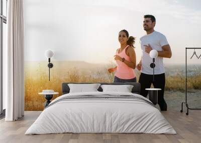 Two athletes running at sunset. Man and woman training together. Wall mural