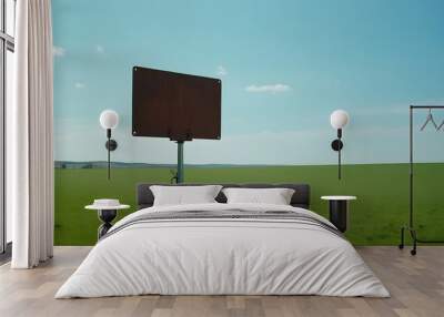 A rusty metal plate mounted on a pole stands alone in a vast, empty green field under a clear blue sky. Wall mural