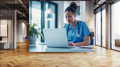 Attentive nurse in scrubs reviewing medical history or patient information on her laptop in clinic office - Science and hospital work concept Wall mural