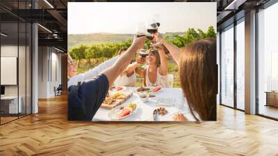 Happy adult friends having fun drinking red wine and eating together with vineyard in background - Multiracial people doing appetizer at summer time in countryside resort - Main focus on hands Wall mural