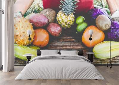 Male farmer with tropical organic fruits and vegetables picked up in greenhouse - Greengrocer with day harvest on rusty wood board Wall mural