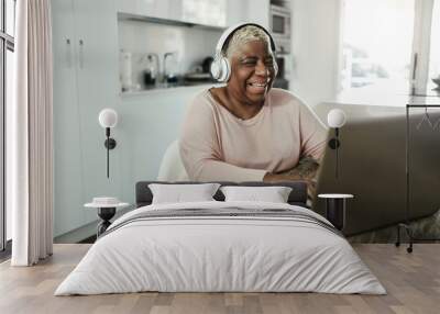 Senior woman using laptop while wearing headphones at home - Joyful elderly lifestyle and technology concept - Focus on face Wall mural