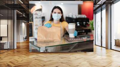 Young woman serving takeaway coffee and breakfast at bakery shop while wearing protective face mask - Delivery service for Coronavirus outbreak concept - Focus on right hand Wall mural