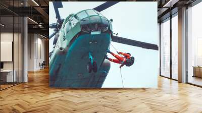 Rescue helicopter and rescuer on the rope - life-saving flying vehicle on the rainy sky background. Wall mural