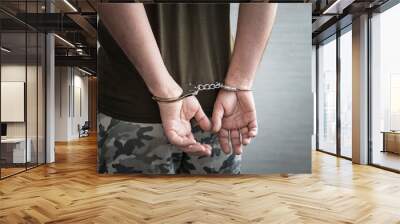 A military soldier in handcuffs, hands behind his back, on a dark background. Concept: war criminal, prisoner of war, officer tribunal. Wall mural