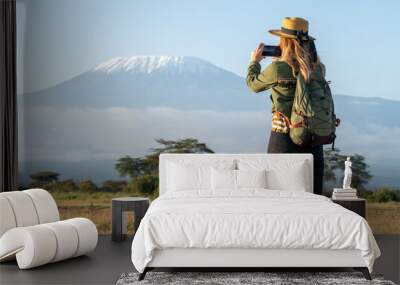 beautiful young girl In a hat stands against the backdrop of the Kilimanjaro volcano and looks away. The concept of tourism and African safari. A female backpacker takes pictures of nature and animals Wall mural