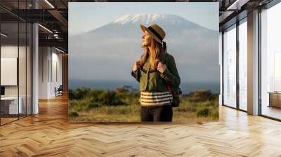 beautiful young girl In a hat stands against the backdrop of the Kilimanjaro volcano and looks away. The concept of tourism and African safari. Wall mural