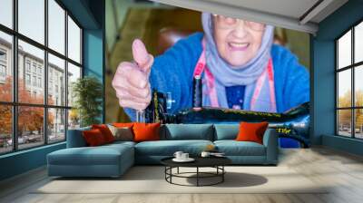 Arabic muslim old woman happy while using sewing machine Wall mural