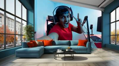 Cheerful young Hispanic man taking a selfie inside a video game room. Wall mural