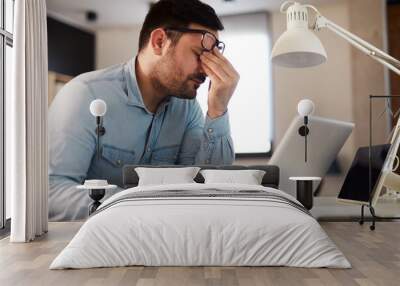  Young man has a headache at work while working on a laptop Wall mural