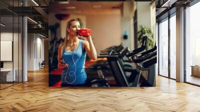 Beautiful young woman resting and drinking water in the gym Wall mural