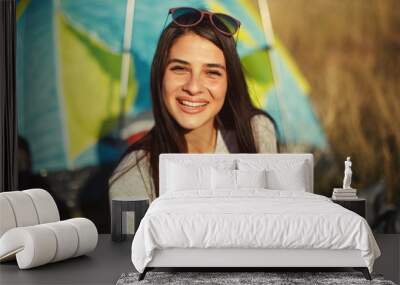 Closeup of happy young woman sitting in front of a tent at camping Wall mural