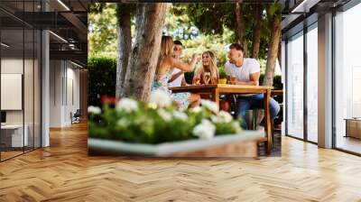 Group of young people sitting at a table in a summer bar laughing and drinking beer Wall mural