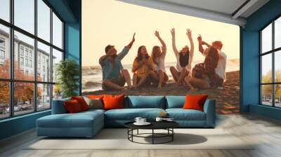 Happy friends sitting on the beach singing and playing guitar during the sunset Wall mural