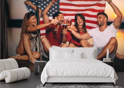 Happy group of young people toasting and hold the American flag on a dock by the river during the summer sunset. Wall mural