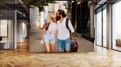 Happy young tourist couple walking through european city with suitcase Wall mural