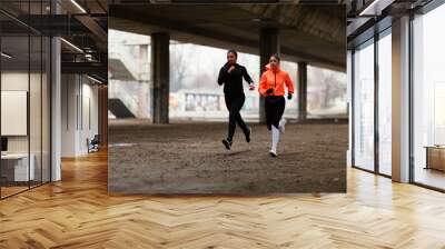 Two young fitness woman running under overpasses during cold day Wall mural