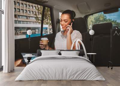 Young businesswoman talking on the phone in the back seat of the car Wall mural