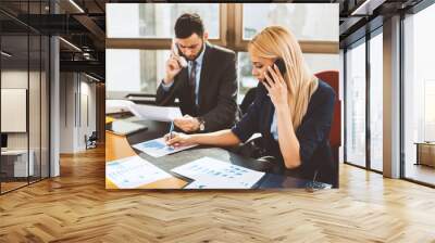 Young businesswoman talking on the phone with business man in the background in the office Wall mural