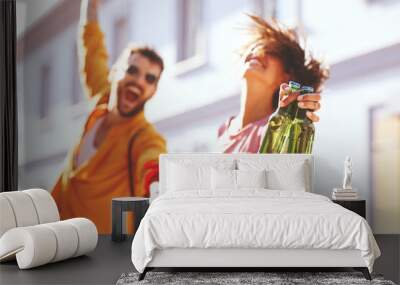 Young couple dancing on the street and holding two bottles of beer. Selective focus on beer. Wall mural