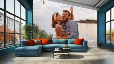 Young couple in love flirting by the river at sunset Wall mural