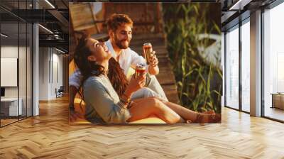 Young happy couple enjoy in beer by the river during the sunset Wall mural