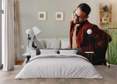 Young man has back pain while working in the office at a desk Wall mural