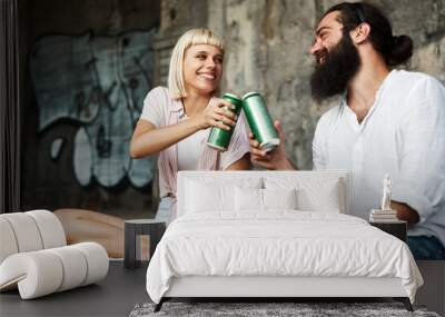 Young smiling couple toasting with beer cans in an urban environment Wall mural